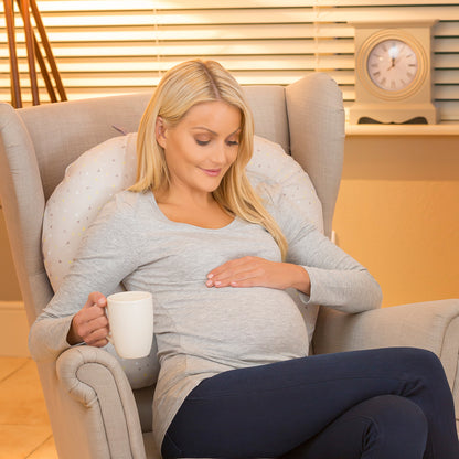 Pregnant mother with nursing pillow at her back sitting in a chair