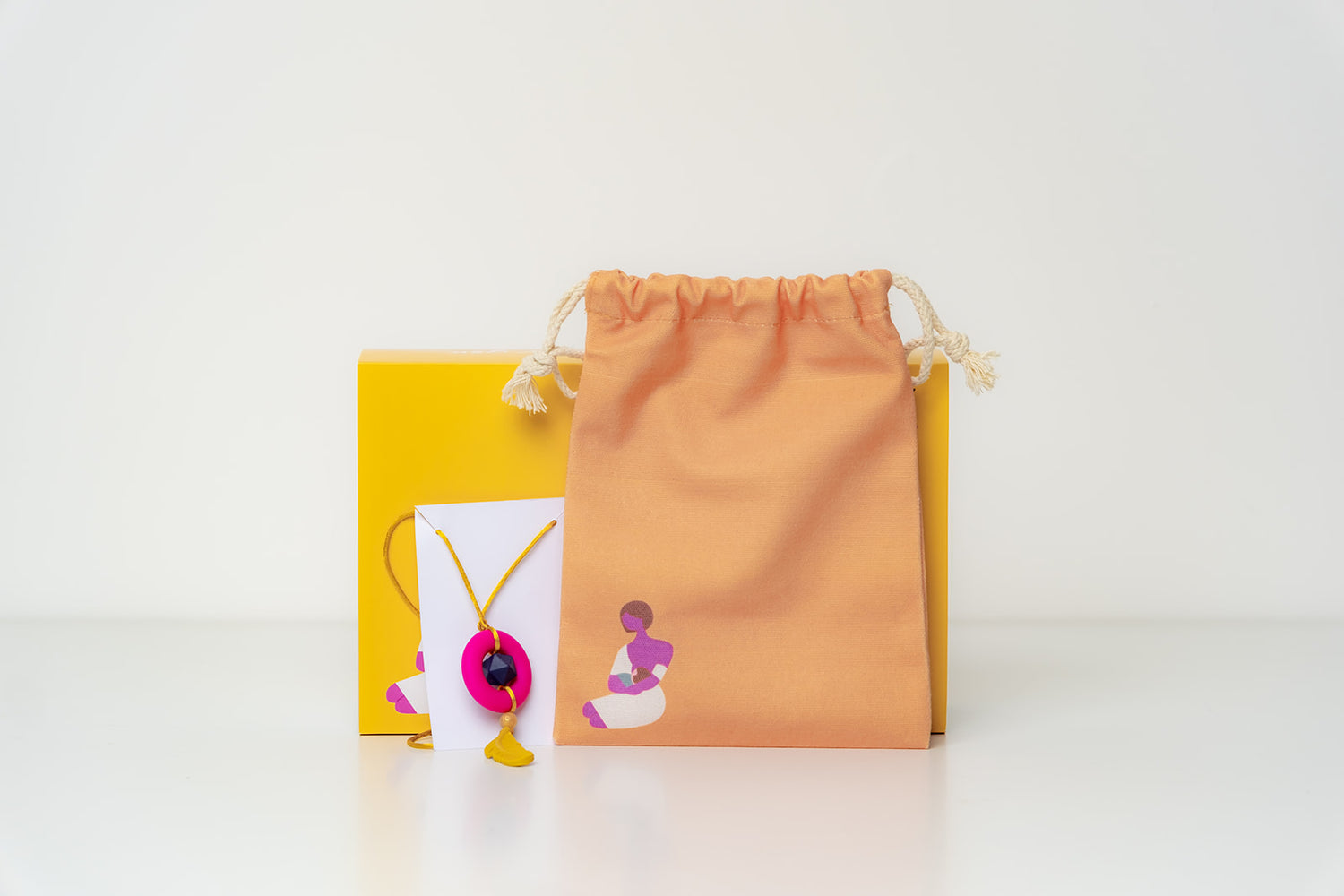 A breastfeeding gift box which includes silicone colourful necklace and a small orange breastfeeding tote bag.