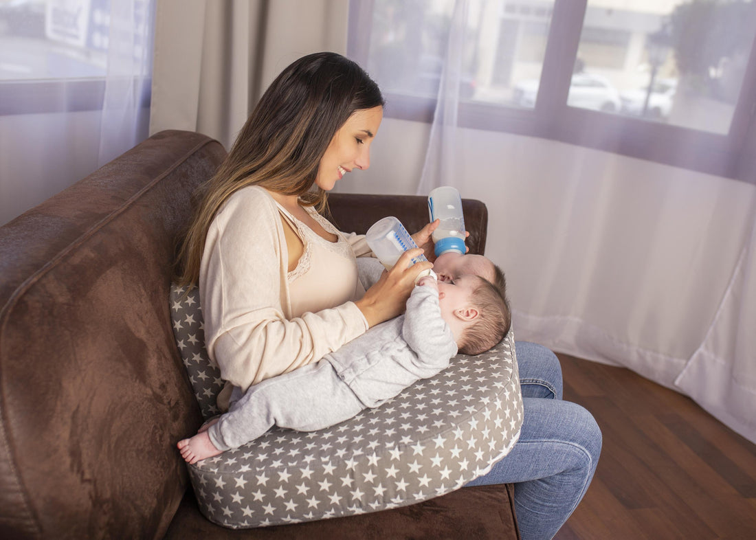 A mother feeding her twin babies bottles, using a twin breastfeeding pillow, wrapped around her middle.